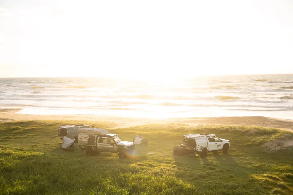 Norweld-equipped 4WD vehicles and canopies set up for camping beside the beach at sunset
