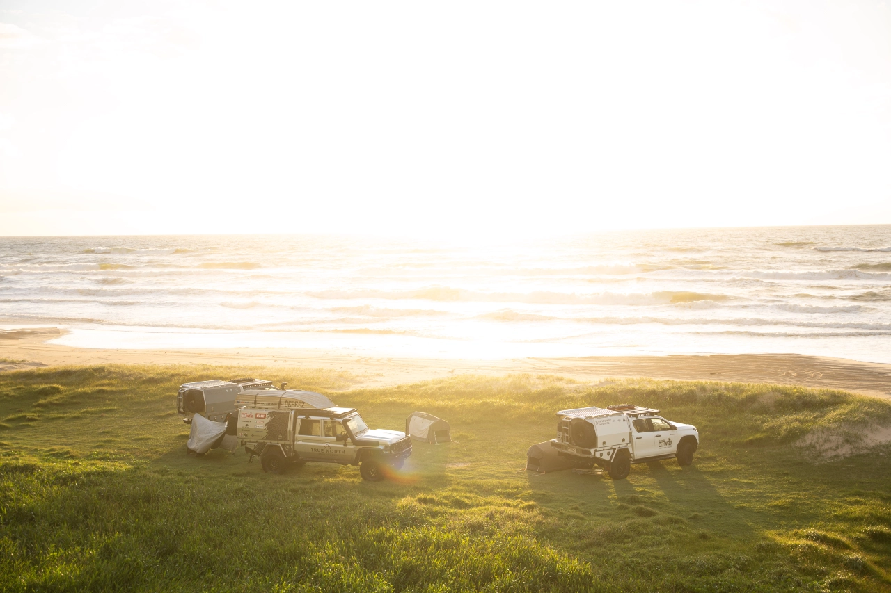 Norweld-equipped 4WD vehicles and canopies set up for camping beside the beach at sunset